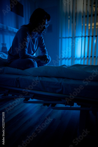 Patient reflects quietly. Hospital bed with contemplative patient. Lone individual sits peacefully in hospital room. Silent patient rests under calming blue illumination overnight