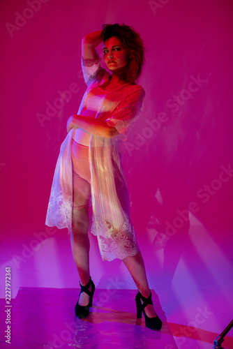 Standing model in lace skirt posing, bold confident stance under magenta studio lighting, hand placed over head, high heels, retro glamour vibe for runway or nightlife campaign