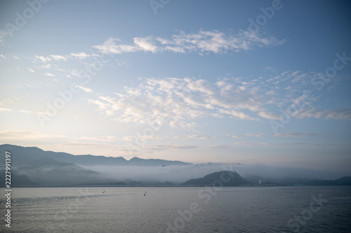 Wide blue sky with clouds over morning fog and sea at dawn