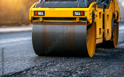 Yellow road roller compacting fresh dark asphalt at ground level