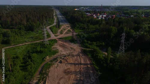 A high-altitude flight over power line poles and a paved road construction site on a sunny summer evening. Eastern Bypass, Novosibirsk, Russia.