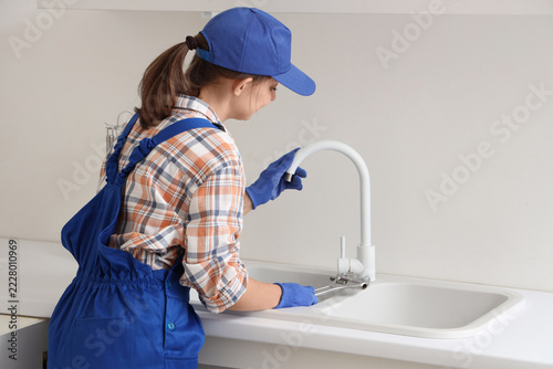 Fotografie Plumbing repair and home maintenance, female plumber fixing a kitchen faucet wit
