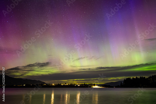 Fotografie Panoramic view of vibrant Aurora Australis with colorful light beams over a calm lake at night, New Zealand