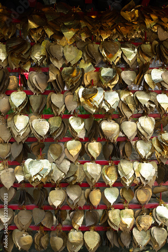 Numerous leaf-shaped metal charms, in varying shades of silver and gold, are hung from a metal bar.