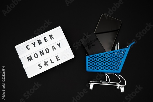 Cyber Monday Sale Flat Lay with Black Gift Boxes, Smartphone, Blue Shopping Cart and Lightbox on Black Background