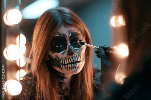 Woman creating halloween skull makeup in a mirror