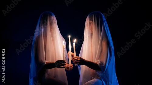 Two ghostly veiled figures holding lit candles in dark setting