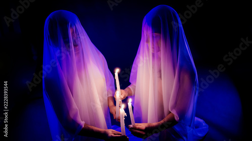 Two ghost figures holding candles in dark illuminated setting