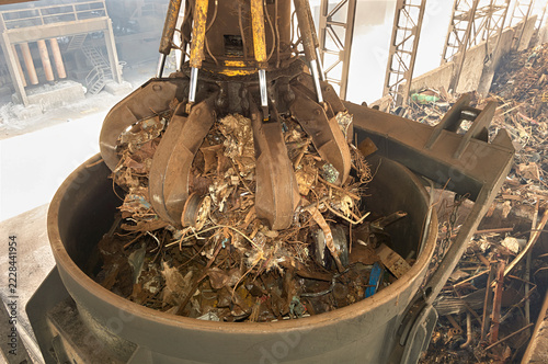 Hydraulic orange peel grabber loading scrap metal into container in steel mill factory