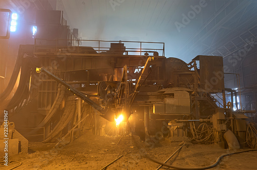 Heavy industrial machinery operating with molten metal and sparks in a dark steel mill factory
