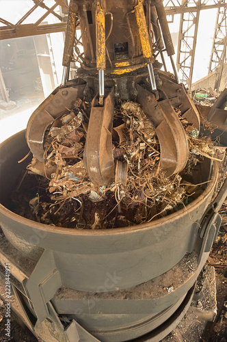 Close up of hydraulic orange peel grabber discharging scrap metal into heavy ladle bucket in steel mill