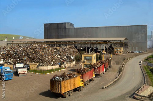 Convoy of dump trucks loaded with scrap metal arriving at a large metal recycling plant and steel mill facility