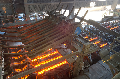 Glowing red hot steel billets processing on a cooling bed machine in a heavy industrial steel mill