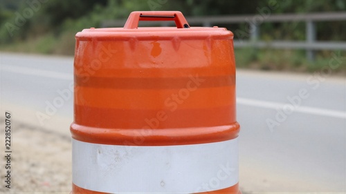Close-up orange traffic barrel with white reflective band and wet scuffed surface at roadside for traffic safety use case