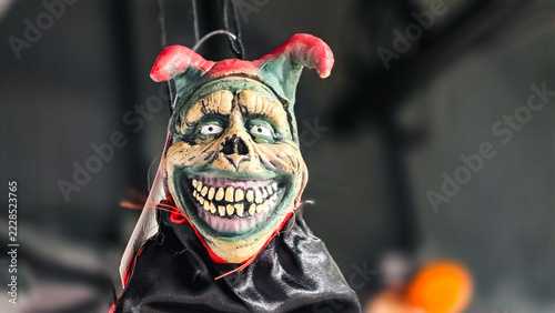 creepy hanging halloween jester clown mask prop with spooky grin monstrous teeth and red horns hanging as decoration

