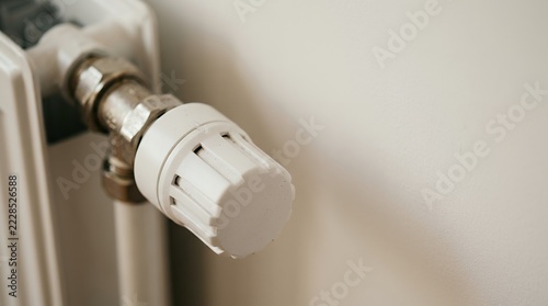 White radiator thermostat valve knob on a clean wall with copy space