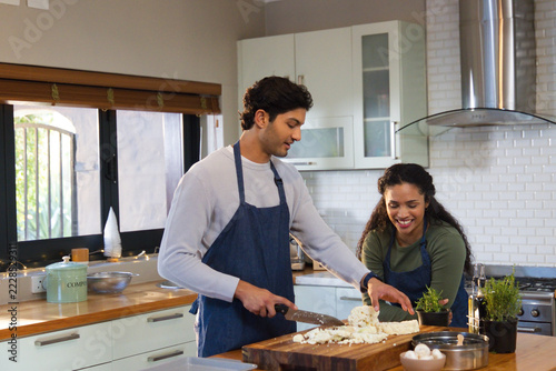 Diverse couple chopping cauliflower with chef's knife on kitchen island pointing