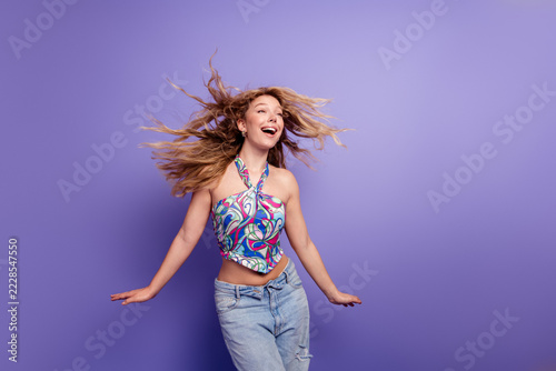 Obraz na plátně Happy young woman dancing in colorful halter top and jeans against a purple back