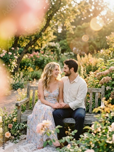 A Couple Enjoys a Serene Sunset in a Lush Garden Sitting on a Bench and Holding Hands