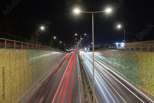 View of long-exposure vehicle light trails along Triq Mikiel Anton Vassalli, a sunken arterial road in Msida, Malta, lined with tiled retaining walls and streetlights at night.