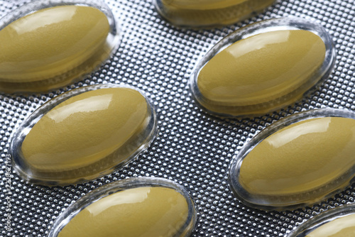 close-up view of oval, yellow capsules or tablets sealed individually within silver, textured metallic blister pack, organized pharmaceutical or dietary product layout, yellow pills in blister pack,