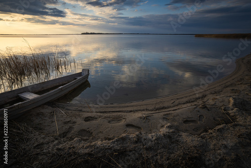 Sunset on the lake. Old rural wooden, fishing boat is moored on the shore of a lake.