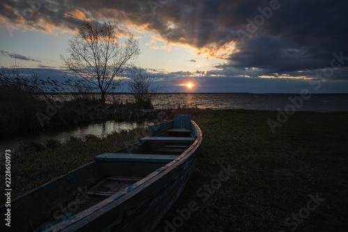 Sunset on the lake. Old rural wooden, fishing boat is moored on the shore of a lake.