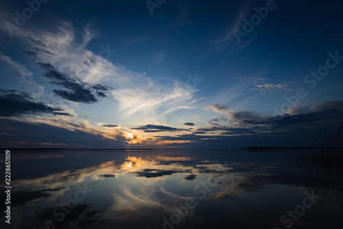 Sunset on the lake. Evening sky with beautiful clouds is reflected in the water of the lake