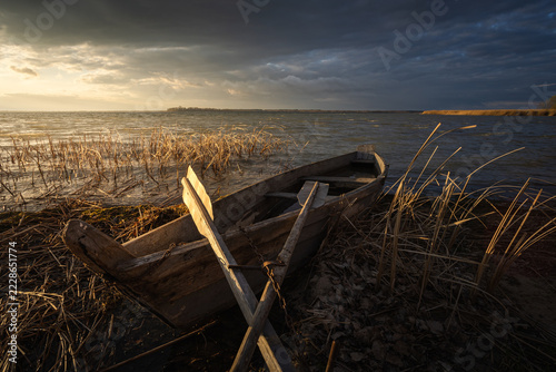 Sunset on the lake. Old rural wooden, fishing boat is moored on the shore of a lake.