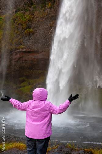 woman standing in front of seljalandsfoss waterfall in south iceland with cliffs surrounding