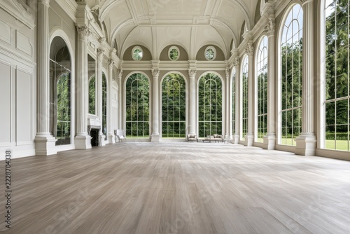 Empty grand neoclassical interior with arched windows, ornate columns, vaulted ceiling, pale walls, and polished wood flooring in a historic conservatory