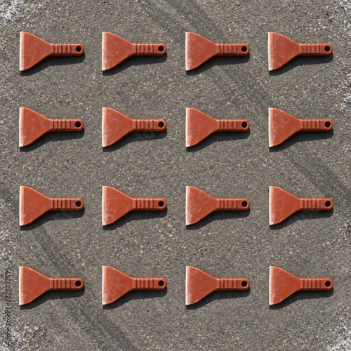 Seasonal car care tools featuring rust-coloured ice scrapers arranged in a grid on weathered grey asphalt for winter vehicle maintenance