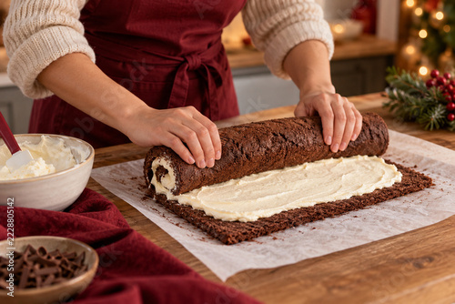 A home baker rolls a chocolate Christmas log cake around a light cream