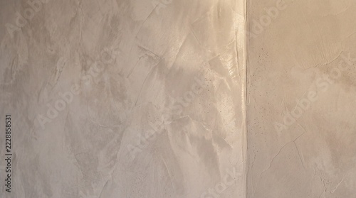 Close-up of a beige decorative Venetian plaster wall corner showing glossy polished texture on the left and matte finish on the right