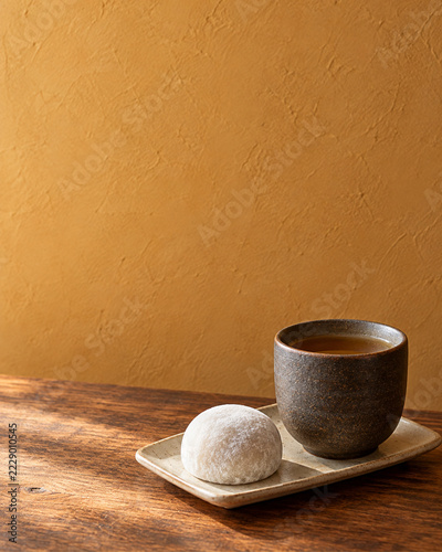 木の卓上に置かれた湯飲みと粉をまぶした餅菓子