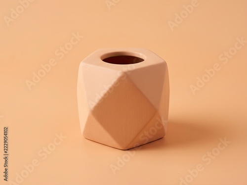 A single, minimalist geometric ceramic vase with a matte finish, presented on a matching monochromatic peach-colored background.