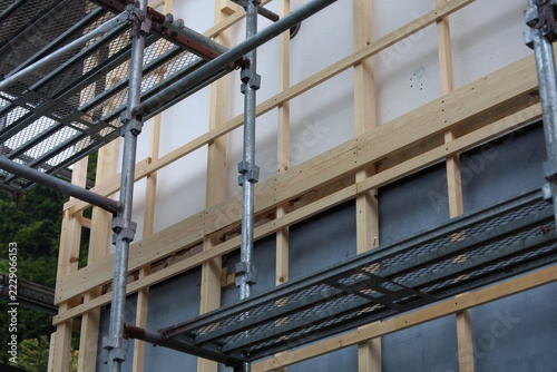 New Vertical Wood Siding and Scaffolding Against Green Trees at Building Renovation Site