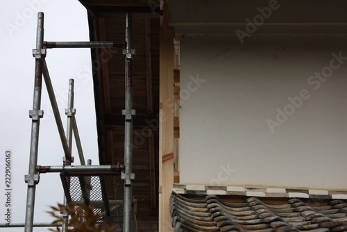 Traditional Japanese Clay Tile Roof Eave with New White Wall and Scaffolding Under Cloudy Sky