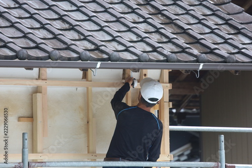 Construction Worker Measuring Roof Eave Area on Scaffolding with Traditional Japanese Curved Tile Roof and Gutter