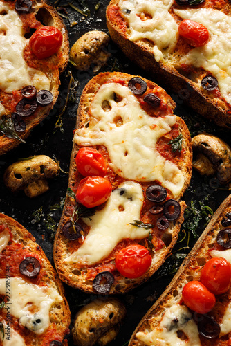 Halloween bruschetta toasts with ghost shaped melted cheese, cherry tomatoes, black olives and spooky mushrooms, top view