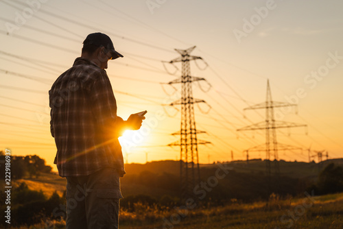 Man Checking Smartphone Beneath Power Lines at Sunset