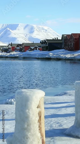 Wooden houses of Longyearbyen town on the snowy shore of the Arctic Ocean with snow-capped mountains in the background in Svalbard Norway
