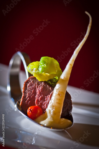 Aperitif spoon featuring an artfully arranged gourmet amuse-bouche: pan-seared beef tenderloin (served medium-rare) with Savoy cabbage and parsnip purée.