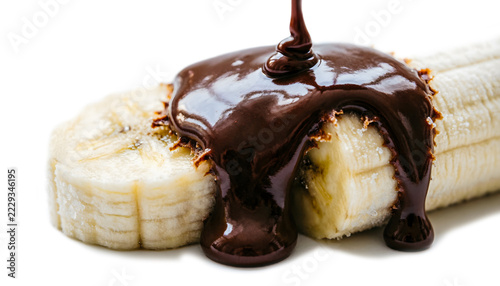 Macro of warm dark chocolate sauce drizzled onto cold frozen slices of banana, instant hardening texture, isolated on a white background.