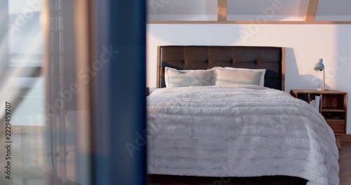 Semi-sheer curtain is drifting from sliding door due to breeze, revealing king bed with comforter