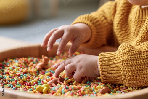 Close-Up of Toddler Hands Exploring Rainbow Sensory Rice Bin with Animal Figurines in Montessori Early Childhood Activity