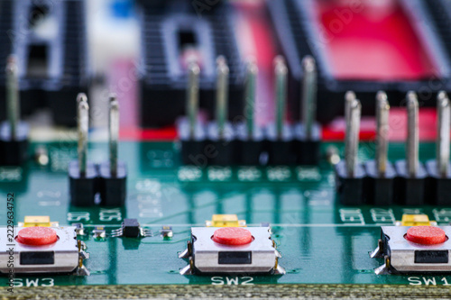 Close up macro shot of circuit board with red push buttons and pin headers