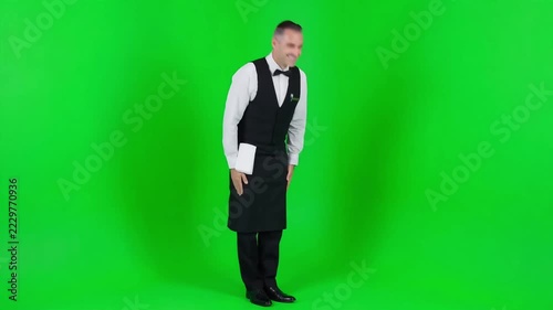 Professional waiter in uniform bowing politely with respectful gesture against bright green screen chroma background