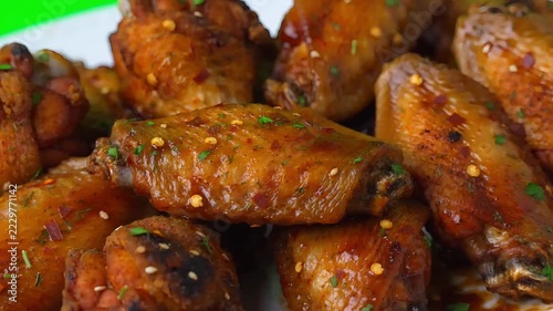 Delicious spicy chicken wings coated in savory glaze arranged on white plate with green backdrop