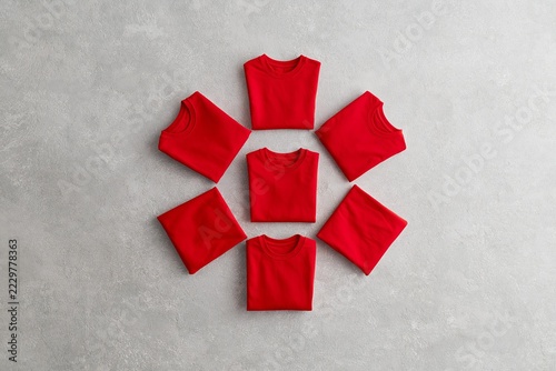 Seven red t-shirts arranged in a circle on a textured grey background, suggesting organization and minimalism